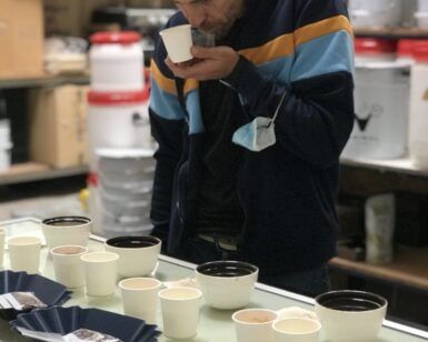 Inmerso en una mesa de cafés de especialidad y abastos, una persona saborea el aroma de su taza, experimentando la esencia de una Cata de cafés de especialidad. - ForTwo - Planes para parejas