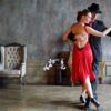 En una sala con poca luz, adornada con flores y decoración vintage, una pareja baila tango con gracia, capturando la pasión de las famosas Clases de Baile en Sevilla de Sevilla: Flamenco, Ballet, Sevillanas, Bailes Latinos y de Salón. - ForTwo - Planes para parejas