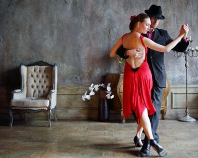En una sala con poca luz, adornada con flores y decoración vintage, una pareja baila tango con gracia, capturando la pasión de las famosas Clases de Baile en Sevilla de Sevilla: Flamenco, Ballet, Sevillanas, Bailes Latinos y de Salón. - ForTwo - Planes para parejas