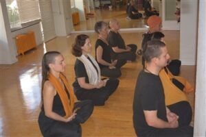 Vestidos de negro, la gente se sienta con las piernas cruzadas y medita en una habitación luminosa, abrazando el bienestar a través de Clases de Yoga Terapéutico en Granada: bienestar para cuerpo y mente. - ForTwo - Planes para parejas