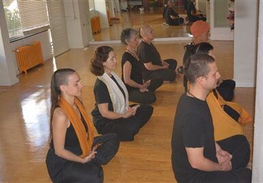 Vestidos de negro, la gente se sienta con las piernas cruzadas y medita en una habitación luminosa, abrazando el bienestar a través de Clases de Yoga Terapéutico en Granada: bienestar para cuerpo y mente. - ForTwo - Planes para parejas