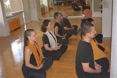 Vestidos de negro, la gente se sienta con las piernas cruzadas y medita en una habitación luminosa, abrazando el bienestar a través de Clases de Yoga Terapéutico en Granada: bienestar para cuerpo y mente. - ForTwo - Planes para parejas
