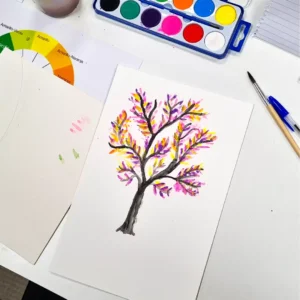 Un colorido cuadro de árbol con hojas otoñales, rodeado de acuarelas y pinceles, invita a un viaje inspirado en el Curso de Iniciación a la Acuarela en Granada: libera tu creatividad artística. - ForTwo - Planes para parejas