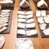 Una variedad de quesos en lonchas bellamente dispuestos en tablas de pizarra, con dos etiquetas de queso en primer plano, complementa perfectamente un entorno inspirado en Barcelona para un Curso de Maridaje de Vinos en Barcelona: Quesos, Ibéricos o Chocolate. - ForTwo - Planes para parejas