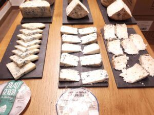 Una variedad de quesos en lonchas bellamente dispuestos en tablas de pizarra, con dos etiquetas de queso en primer plano, complementa perfectamente un entorno inspirado en Barcelona para un Curso de Maridaje de Vinos en Barcelona: Quesos, Ibéricos o Chocolate. - ForTwo - Planes para parejas