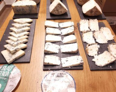Una variedad de quesos en lonchas bellamente dispuestos en tablas de pizarra, con dos etiquetas de queso en primer plano, complementa perfectamente un entorno inspirado en Barcelona para un Curso de Maridaje de Vinos en Barcelona: Quesos, Ibéricos o Chocolate. - ForTwo - Planes para parejas