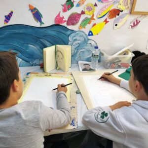 En una mesa rodeada de adornos de peces en El Astillero, dos niños desarrollan sus habilidades creativas, inspirados en los Cursos Anuales de Habilidades Creativas y Pintura que allí se ofrecen. - ForTwo - Planes para parejas