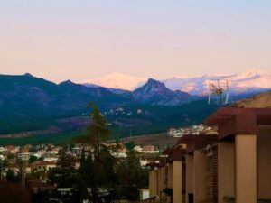 Un paisaje montañoso con picos nevados a lo lejos domina la encantadora ciudad de Granada al atardecer, reflejando la esencia de Degustación de Vinos y Quesos de Granada: Sabores Auténticos para Dos. - ForTwo - Planes para parejas