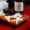 Disfrute de una deliciosa tabla de quesos acompañada de uvas y vino, bellamente colocada sobre un mantel rojo, con la "Degustación de Vinos y Quesos de Granada: Sabores Auténticos para Dos". - ForTwo - Planes para parejas