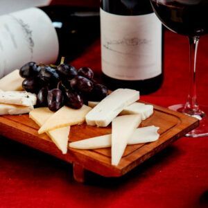 Disfrute de una deliciosa tabla de quesos acompañada de uvas y vino, bellamente colocada sobre un mantel rojo, con la "Degustación de Vinos y Quesos de Granada: Sabores Auténticos para Dos". - ForTwo - Planes para parejas