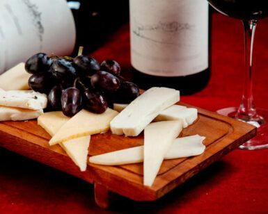 Disfrute de una deliciosa tabla de quesos acompañada de uvas y vino, bellamente colocada sobre un mantel rojo, con la "Degustación de Vinos y Quesos de Granada: Sabores Auténticos para Dos". - ForTwo - Planes para parejas