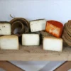 Una selección de Degustación de quesos artesanos en Quesería Cortijo El Aserradero (Granada) adorna un banco de madera, enmarcado por cestas tejidas al fondo. Elaborado artesanalmente con cuidado, cada queso narra la historia de la Quesería Cortijo El Aserradero en la pintoresca Granada. - ForTwo - Planes para parejas