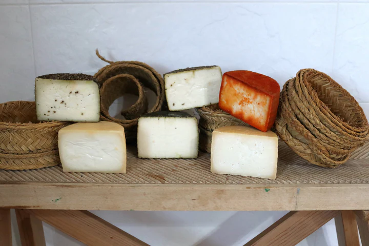 Una selección de Degustación de quesos artesanos en Quesería Cortijo El Aserradero (Granada) adorna un banco de madera, enmarcado por cestas tejidas al fondo. Elaborado artesanalmente con cuidado, cada queso narra la historia de la Quesería Cortijo El Aserradero en la pintoresca Granada. - ForTwo - Planes para parejas