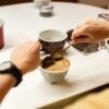 En una pintoresca mesa de Barcelona, alguien utiliza delicadamente dos cucharas para saborear los matices de sabores durante una Cata de Café Abierta en Barcelona: ¡Descubre los Secretos del Café con Cafés el Magnífico!. - ForTwo - Planes para parejas