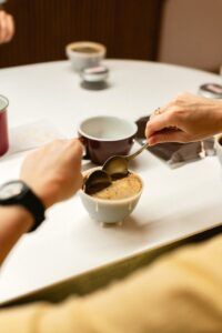 En una pintoresca mesa de Barcelona, alguien utiliza delicadamente dos cucharas para saborear los matices de sabores durante una Cata de Café Abierta en Barcelona: ¡Descubre los Secretos del Café con Cafés el Magnífico!. - ForTwo - Planes para parejas