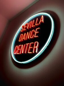 Un vibrante letrero de neón brilla suavemente en una pared tenue, anunciando el Sevilla Dance Center: Academia de baile urbano en el corazón de Sevilla. - ForTwo - Planes para parejas