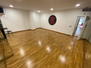 El Sevilla Dance Center, ubicado en el corazón de la ciudad, cuenta con un vibrante estudio de danza con un elegante suelo de madera, una pared de espejos y una silla. El icónico logotipo adorna el espacio, haciéndolo perfecto para los amantes de la danza urbana. - ForTwo - Planes para parejas