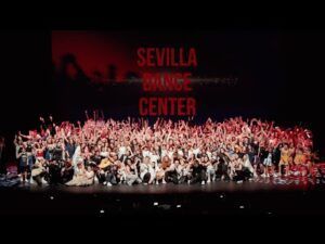 Un gran grupo celebra en el escenario bajo el cartel del Sevilla Dance Center, destacando el espíritu vibrante de la academia de baile urbano en el corazón de Sevilla. - ForTwo - Planes para parejas