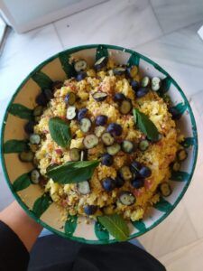 Una ración del "Taller de Cocina Batch Cooking saludable en Sevilla": ensalada de cuscús adornada con arándanos y menta, presentada en una fuente con estampado verde y blanco. - ForTwo - Planes para parejas