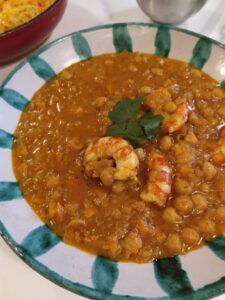 Disfruta de un plato de curry de garbanzos y gambas, con cilantro como aderezo, ideal para cocinar por lotes. Servido a la perfección en un tazón verde y blanco, forma parte de la experiencia de Taller de Cocina Batch Cooking saludable en Sevilla. - ForTwo - Planes para parejas