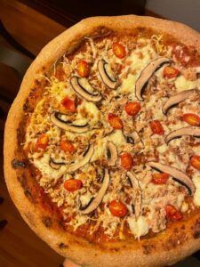 Experimente el sabor sevillano con nuestra pizza Taller de Comida Rápida Saludable, cubierta con tomates cherry, champiñones, queso y carne deshebrada sobre una superficie de madera. Esta deliciosa combinación deleitará su paladar, manteniendo la calidad y el sabor. - ForTwo - Planes para parejas