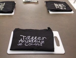 Delantales negros con el texto "Taller de Pasta Fresca en Sevilla" descansan sobre tablas de cortar blancas, capturando la esencia del espíritu culinario de Sevilla. - ForTwo - Planes para parejas