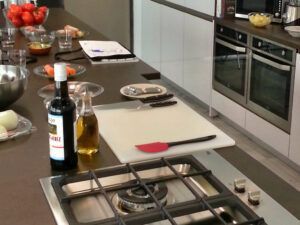Una cocina sevillana, decorada con fogones, tabla de cortar, aceite de oliva, una botella de vino y verduras vibrantes, prepara el escenario para el "Taller de Pasta Fresca en Sevilla", transformando los esfuerzos culinarios en talleres inolvidables. - ForTwo - Planes para parejas