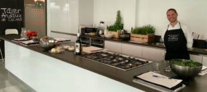 En una acogedora cocina de Sevilla, un hombre, con delantal y rodeado de verduras y hierbas frescas, se encuentra en su puesto de cocina. Con una cálida sonrisa, se dispone a preparar con maestría un delicioso sushi en el Taller de Sushi en Sevilla. - ForTwo - Planes para parejas