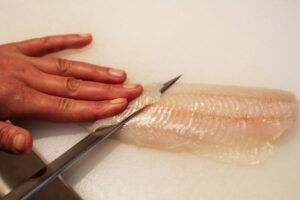 Cortando a mano filetes de pescado crudo con un cuchillo afilado sobre una tabla de cortar blanca en Taller de Sushi en Sevilla para crear exquisitos sabores de sushi. - ForTwo - Planes para parejas