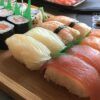 El Taller de Sushi en Sevilla ofrece un surtido de nigiri y maki rolls en bandeja de madera adornados con hojas verdes, capturando la esencia de la cocina japonesa. - ForTwo - Planes para parejas