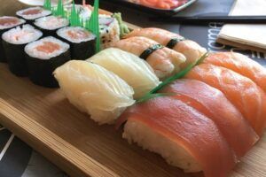 El Taller de Sushi en Sevilla ofrece un surtido de nigiri y maki rolls en bandeja de madera adornados con hojas verdes, capturando la esencia de la cocina japonesa. - ForTwo - Planes para parejas