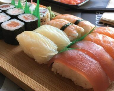 El Taller de Sushi en Sevilla ofrece un surtido de nigiri y maki rolls en bandeja de madera adornados con hojas verdes, capturando la esencia de la cocina japonesa. - ForTwo - Planes para parejas