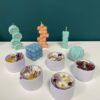Las velas coloridas y de formas únicas de Taller de Velas Decorativas en Granada adornan hermosamente una mesa blanca contra una pared verde azulado, infundiendo su espacio con la esencia de Granada. - ForTwo - Planes para parejas