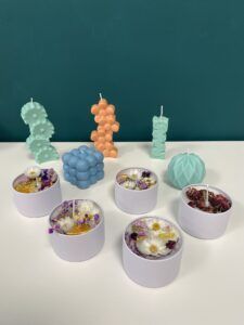 Las velas coloridas y de formas únicas de Taller de Velas Decorativas en Granada adornan hermosamente una mesa blanca contra una pared verde azulado, infundiendo su espacio con la esencia de Granada. - ForTwo - Planes para parejas
