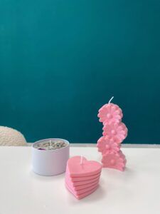 Velas decorativas rosas con forma de flores y corazones acompañan a una vela blanca adornada con pétalos sobre una superficie lisa, capturando el encanto de Granada. Inspirado en Taller de Velas Decorativas en Granada: crea tus propias velas aromáticas. - ForTwo - Planes para parejas