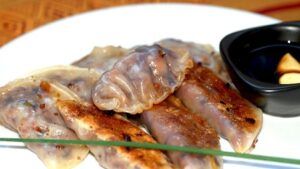 Los dumplings fritos, inspirados en los vibrantes sabores del Taller de cocina japonesa en Sevilla, se presentan en un plato blanco con una sabrosa salsa para mojar. - ForTwo - Planes para parejas