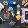 El producto "Talleres de Manualidades en Granada: Crea y Conecta con el Arte" ofrece materiales para manualidades como hilo, botones, pinturas y pinceles sobre una mesa que captura el espíritu artístico de Granada. - ForTwo - Planes para parejas