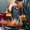 En Espai Granada, el chef cocina hábilmente una gran sartén de arroces humeantes durante los Talleres de cocina con arroces en Espai Granada, cautivando a los espectadores con el rico aroma y los colores vibrantes de los mariscos. - ForTwo - Planes para parejas