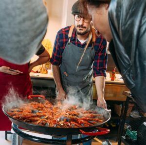 En Espai Granada, el chef cocina hábilmente una gran sartén de arroces humeantes durante los Talleres de cocina con arroces en Espai Granada, cautivando a los espectadores con el rico aroma y los colores vibrantes de los mariscos. - ForTwo - Planes para parejas