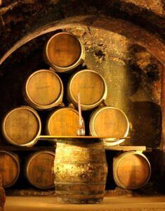 Los barriles de vino se apilan en la bodega rústica de la Bodega Tradicional en Granada, exhibiendo una jarra de vidrio sobre una mesa de barril, complementando la "Visita a Bodega Tradicional en Granada: Un paseo por los secretos del vino. - ForTwo - Planes para parejas