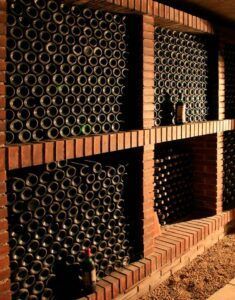 Visita a una Bodega Tradicional en Granada: Un paseo por los secretos del vino cuenta con una encantadora bodega con estantes de ladrillo rústico que sostienen filas de botellas de vino en sus lados, iluminadas por una luz cálida y tenue que evoca el encanto del viejo mundo de Granada. - ForTwo - Planes para parejas