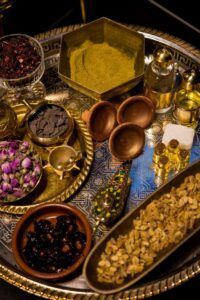 Una bandeja decorativa muestra especias, aceites y flores secas en cuencos y frascos sobre un fondo texturizado inspirado en el Baño Turco con Café y Chocolate en Madrid. - ForTwo - Planes para parejas