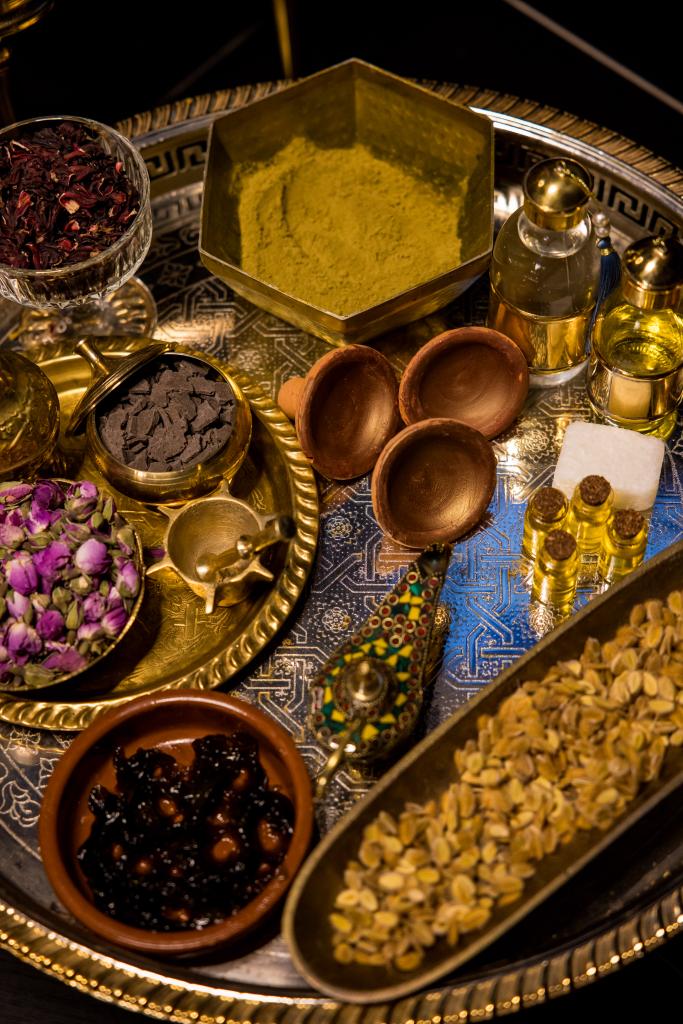 Una bandeja decorativa muestra especias, aceites y flores secas en cuencos y frascos sobre un fondo texturizado inspirado en el Baño Turco con Café y Chocolate en Madrid. - ForTwo - Planes para parejas