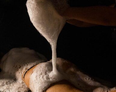 En una sala poco iluminada, una persona se relaja en una mesa, rodeada de relajantes burbujas durante un placentero masaje con espuma, que recuerda la experiencia de lujo que ofrece el Baño Turco con Café y Chocolate en Madrid. - ForTwo - Planes para parejas