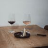 En una mesa de madera en Madrid, dos copas de vino tinto y rosado se combinan con cuñas de queso y un cuchillo en un plato negro: una cata de quesos con maridaje perfecta. - ForTwo - Planes para parejas