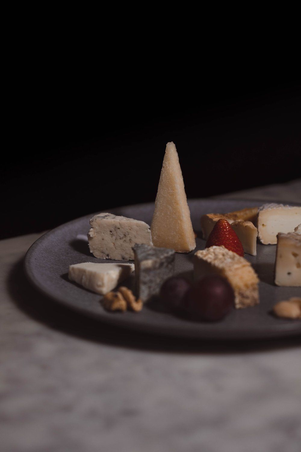 La tabla "Cata de quesos con maridaje en Madrid" presenta una selección de quesos con uvas, una fresa y nueces sobre una superficie oscura, reflejando la rica herencia culinaria de Madrid. - ForTwo - Planes para parejas
