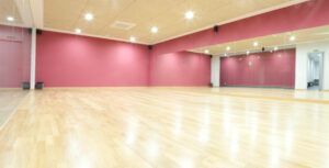 Un espacioso estudio de baile con suelo de madera, paredes rojas y grandes espejos en un lateral es perfecto para clases de baile de salón en Madrid: ritmos latinos, swing y tango. Las brillantes luces del techo crean un ambiente ideal. - ForTwo - Planes para parejas