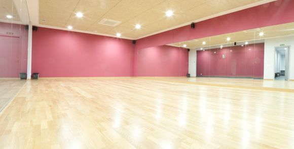 Un espacioso estudio de baile con suelo de madera, paredes rojas y grandes espejos en un lateral es perfecto para clases de baile de salón en Madrid: ritmos latinos, swing y tango. Las brillantes luces del techo crean un ambiente ideal. - ForTwo - Planes para parejas