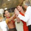 Tres personas bailan alegremente en un espacio cerrado, con dos mujeres y un hombre sonriendo y uniendo las manos, encarnando el espíritu animado de una sesión improvisada en Clases de Baile en Madrid: Salsa, Bachata, Tango y Más en Studio11. - ForTwo - Planes para parejas