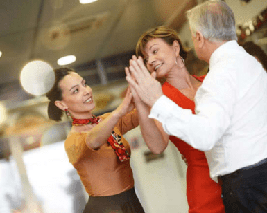 Tres personas bailan alegremente en un espacio cerrado, con dos mujeres y un hombre sonriendo y uniendo las manos, encarnando el espíritu animado de una sesión improvisada en Clases de Baile en Madrid: Salsa, Bachata, Tango y Más en Studio11. - ForTwo - Planes para parejas